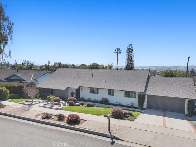 ranch-style house with driveway, roof with shingles, an attached garage, and a front yard