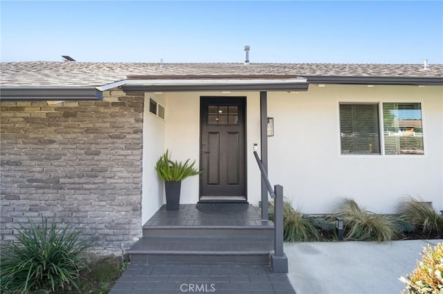 view of exterior entry featuring a shingled roof, stone siding, and stucco siding