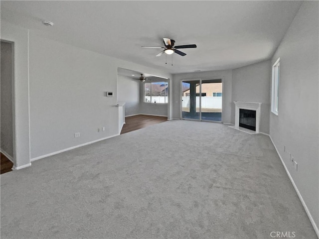 unfurnished living room with carpet, a fireplace with flush hearth, a ceiling fan, and baseboards