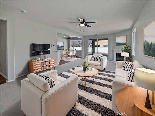 living room with carpet floors, ceiling fan, a fireplace, and baseboards