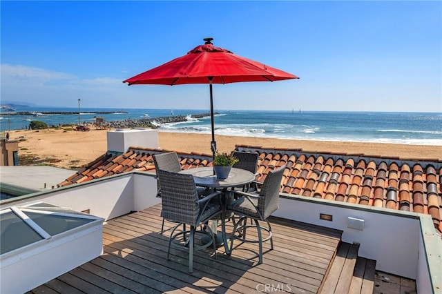 wooden deck with outdoor dining area, a view of the beach, and a water view