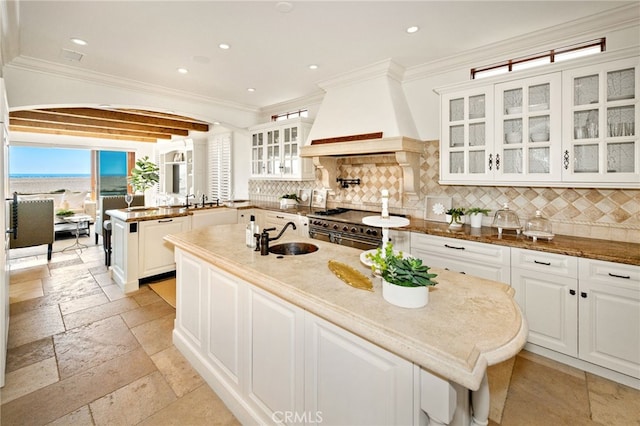 kitchen with range with two ovens, a peninsula, a sink, custom exhaust hood, and stone tile flooring