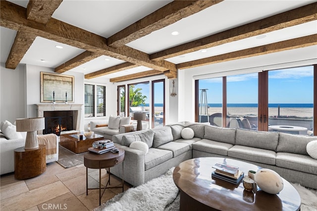 living area featuring beamed ceiling, a water view, a lit fireplace, and a healthy amount of sunlight