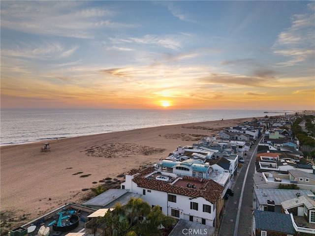 aerial view at dusk featuring a water view and a beach view