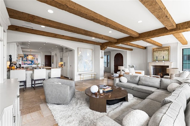 living area featuring arched walkways, beamed ceiling, and a lit fireplace