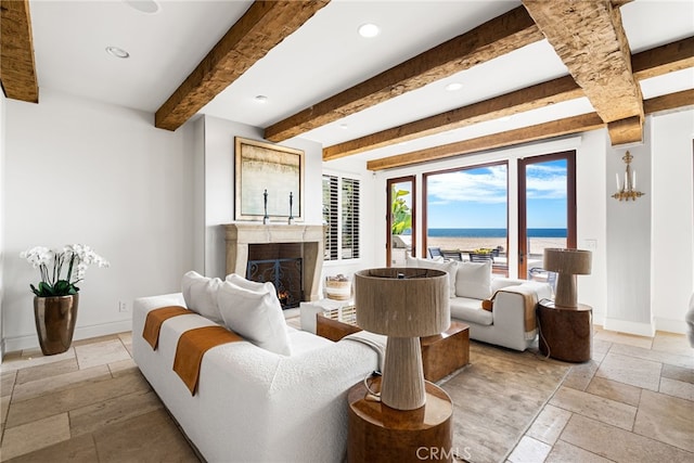 living area featuring a lit fireplace, beamed ceiling, stone tile flooring, and baseboards