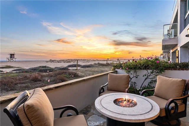 balcony at dusk featuring an outdoor fire pit and a water view
