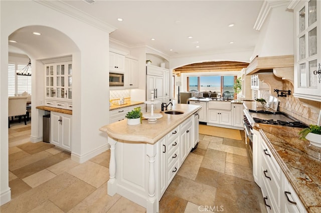 kitchen with a sink, appliances with stainless steel finishes, tasteful backsplash, a center island with sink, and custom range hood