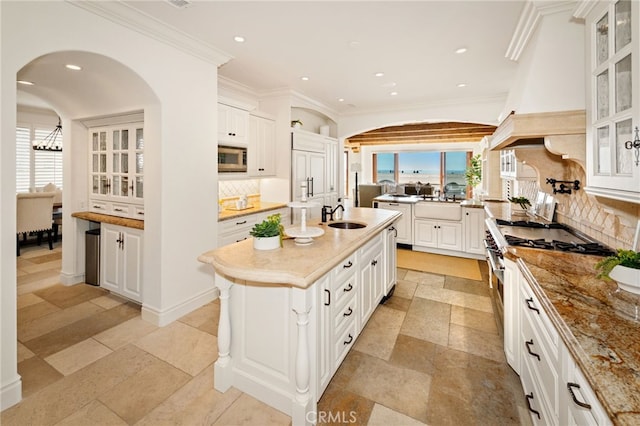kitchen with white cabinets, stainless steel appliances, backsplash, a sink, and a center island with sink