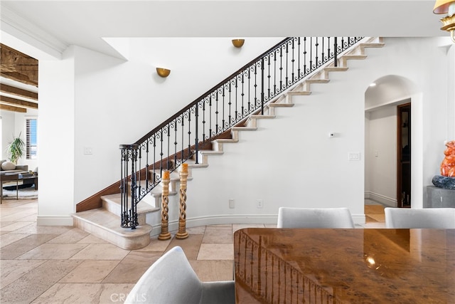 stairs featuring stone tile floors, baseboards, arched walkways, and beamed ceiling