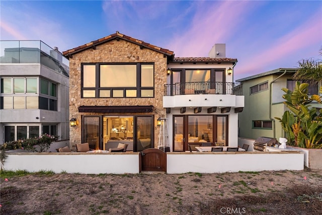 back of property featuring a chimney, a tile roof, stone siding, and a balcony