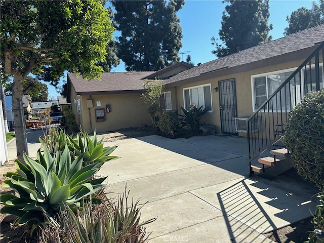 view of front facade featuring a shingled roof, a patio area, fence, and stucco siding