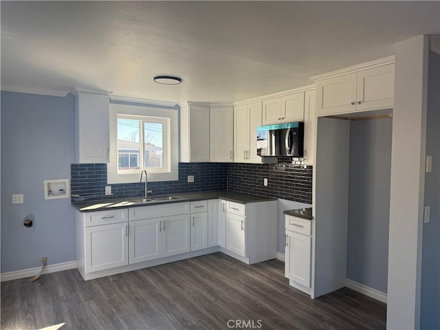 kitchen with dark wood-style floors, dark countertops, stainless steel microwave, decorative backsplash, and a sink