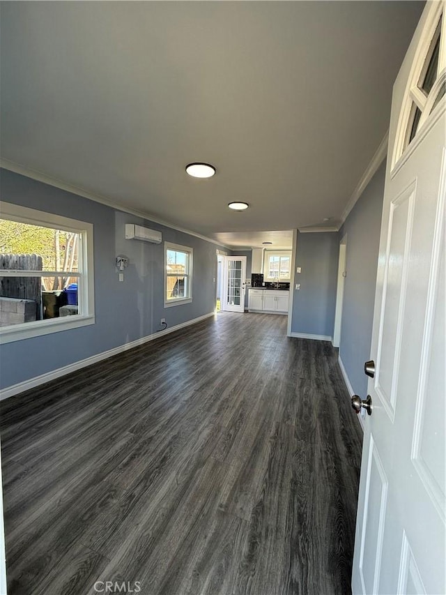 unfurnished living room with dark wood-style floors, a wall mounted AC, ornamental molding, a healthy amount of sunlight, and baseboards