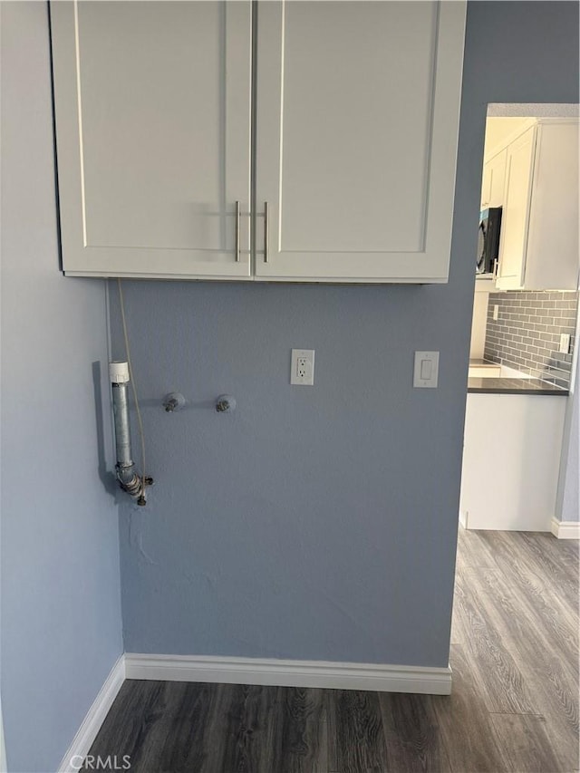 clothes washing area with dark wood-style floors, cabinet space, and baseboards