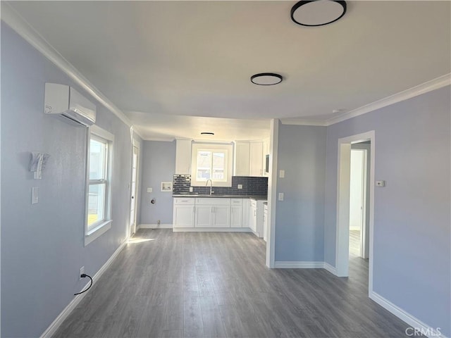 kitchen with wood finished floors, white cabinetry, a wall mounted AC, decorative backsplash, and crown molding