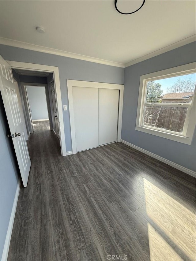 unfurnished bedroom featuring ornamental molding, dark wood-style flooring, a closet, and baseboards