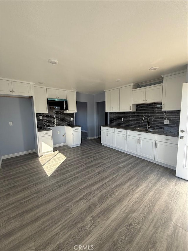 kitchen featuring dark countertops, stainless steel microwave, dark wood finished floors, and a sink