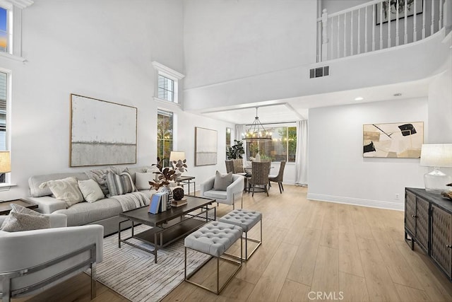 living area featuring visible vents, plenty of natural light, light wood-style flooring, and an inviting chandelier