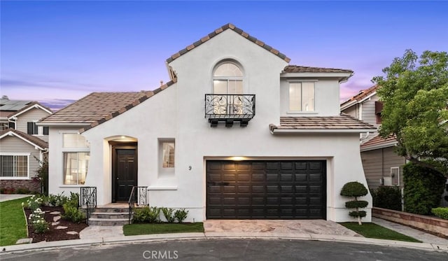 mediterranean / spanish house featuring a garage, concrete driveway, a balcony, a tiled roof, and stucco siding