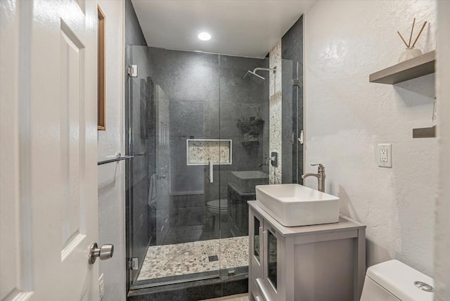 full bath featuring a shower stall, a textured wall, vanity, and toilet