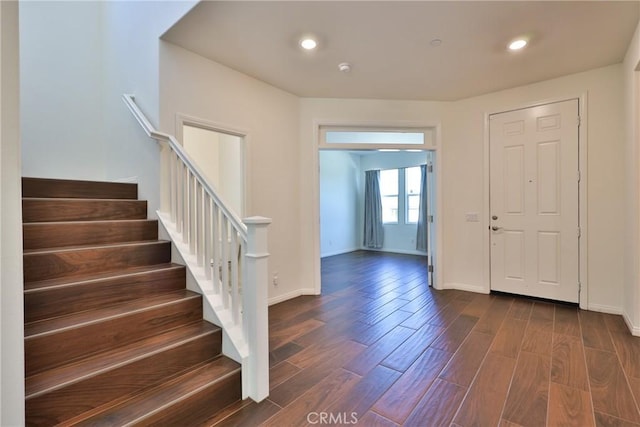 foyer with dark wood finished floors, baseboards, and stairs