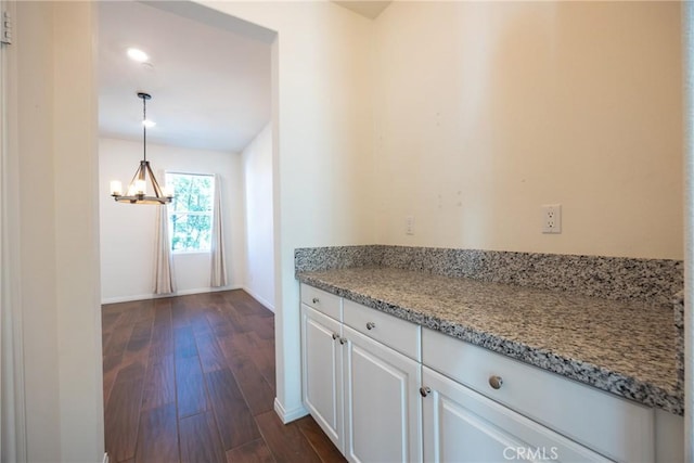 kitchen with baseboards, white cabinets, light stone counters, dark wood-type flooring, and a notable chandelier