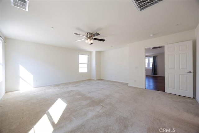 carpeted empty room featuring a healthy amount of sunlight, ceiling fan, and visible vents