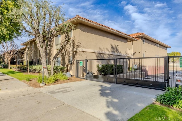 view of property exterior with fence, a tile roof, a gate, and stucco siding