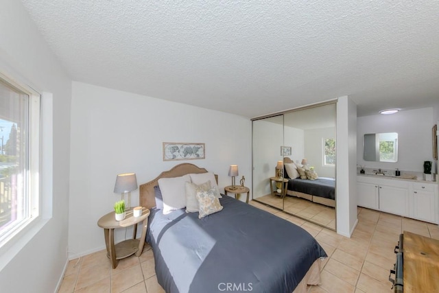 bedroom with light tile patterned floors, a closet, a sink, a textured ceiling, and baseboards