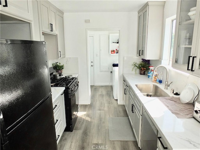 kitchen with light wood-type flooring, black appliances, glass insert cabinets, and a sink