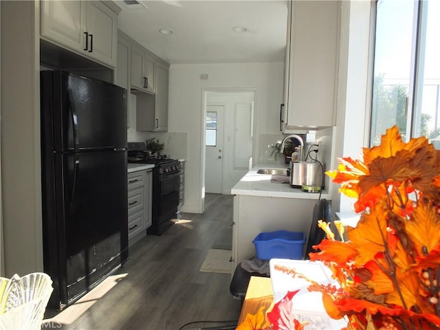 kitchen featuring dark wood-style flooring, gray cabinets, light countertops, a sink, and black appliances