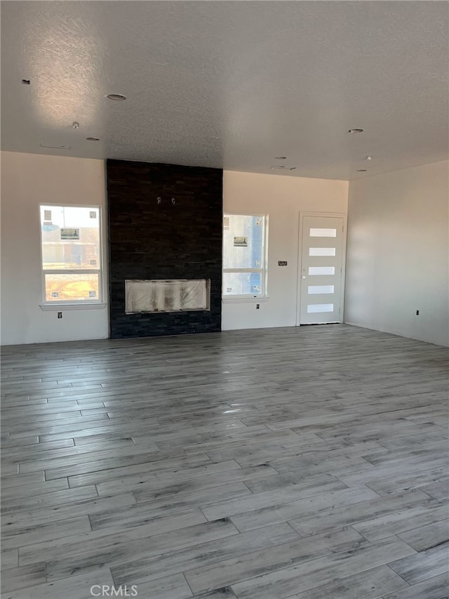 unfurnished living room featuring wood finished floors, a large fireplace, and a textured ceiling