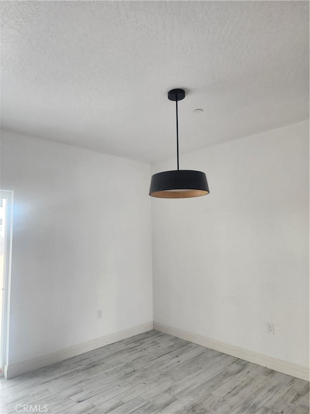 spare room featuring light wood finished floors, baseboards, and a textured ceiling
