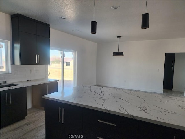 kitchen featuring light stone countertops, backsplash, dark cabinetry, and plenty of natural light