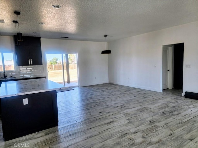 kitchen featuring light wood-type flooring, backsplash, hanging light fixtures, a sink, and dark cabinets