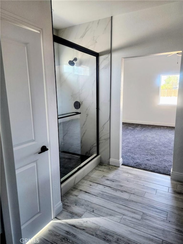 bathroom with a marble finish shower, baseboards, and wood finished floors