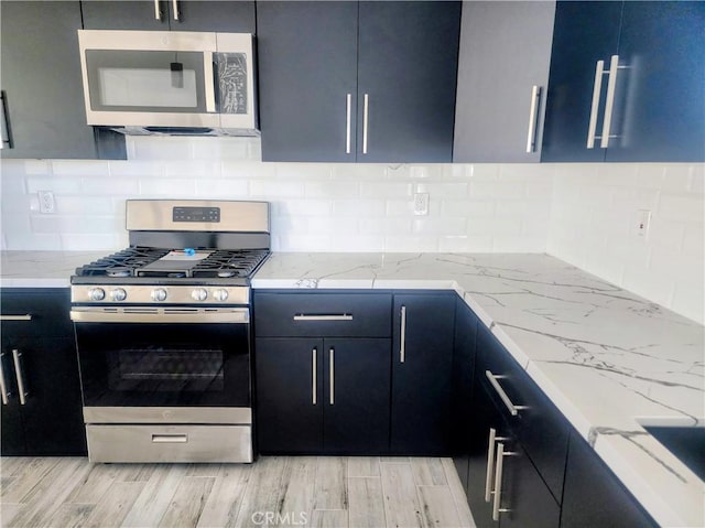 kitchen featuring light stone countertops, light wood-style flooring, tasteful backsplash, and appliances with stainless steel finishes
