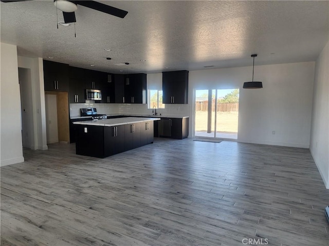 kitchen featuring a kitchen island, stainless steel appliances, dark cabinetry, and open floor plan