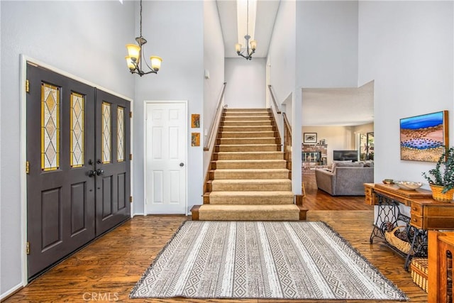 entrance foyer with a chandelier, wood finished floors, stairs, and a towering ceiling