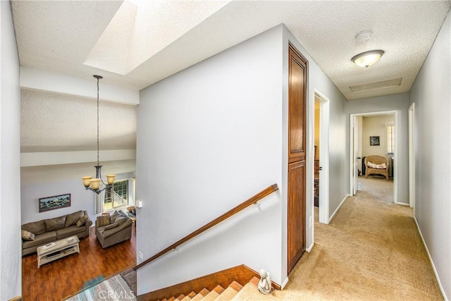 corridor featuring light carpet, baseboards, an inviting chandelier, a textured ceiling, and an upstairs landing