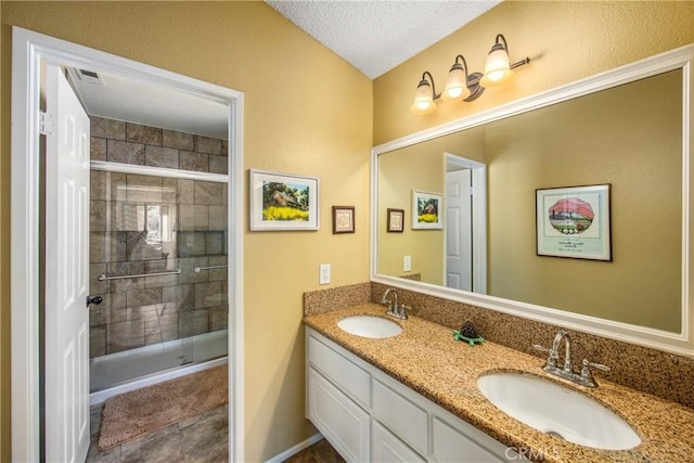 bathroom featuring a textured ceiling, double vanity, a stall shower, and a sink