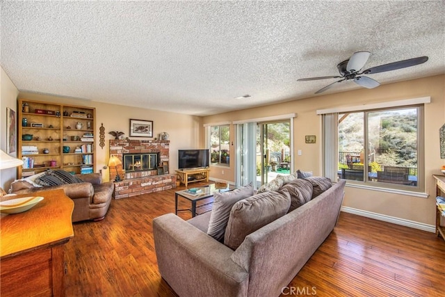 living area with a brick fireplace, ceiling fan, a textured ceiling, wood finished floors, and baseboards