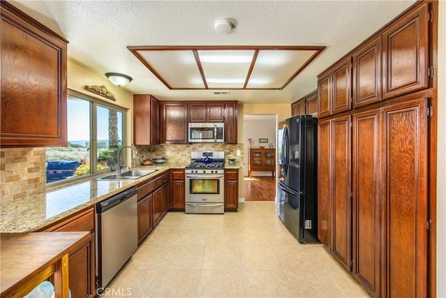 kitchen with light stone counters, light tile patterned floors, stainless steel appliances, backsplash, and a sink