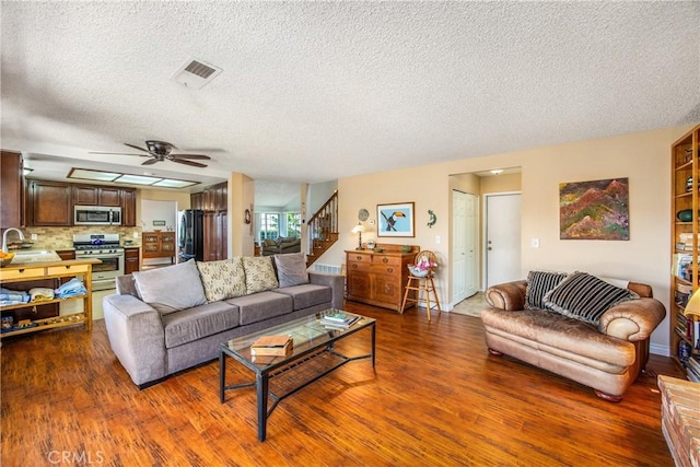 living room featuring a textured ceiling, stairs, visible vents, and wood finished floors