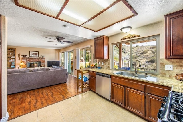 kitchen featuring a sink, range with gas stovetop, stainless steel dishwasher, a brick fireplace, and tasteful backsplash