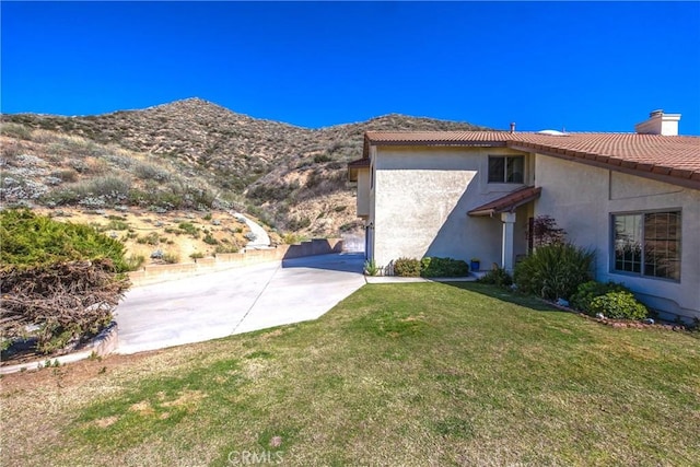 view of side of home with a chimney, stucco siding, a lawn, a mountain view, and a tiled roof