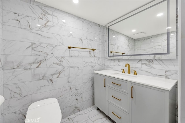 bathroom featuring toilet, marble finish floor, vanity, tile walls, and recessed lighting