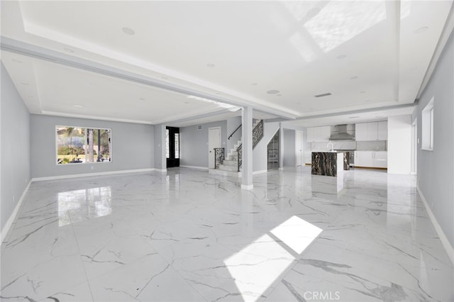 unfurnished living room featuring stairs, marble finish floor, a raised ceiling, and baseboards