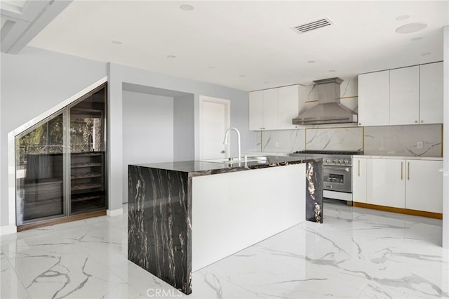 kitchen featuring visible vents, white cabinets, marble finish floor, stainless steel stove, and wall chimney range hood